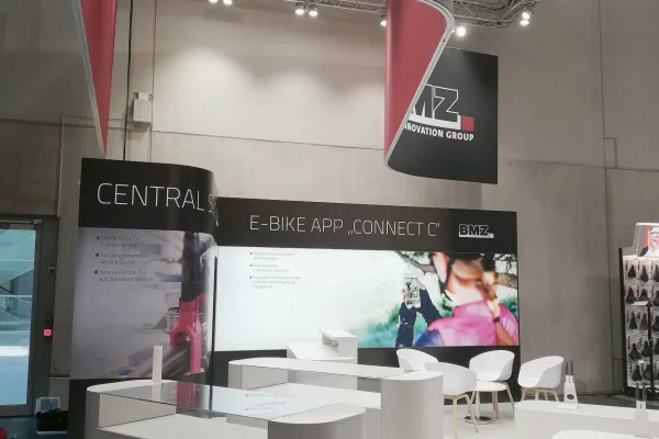 Messestand von BMZ Group mit Tischen, Stühlen.