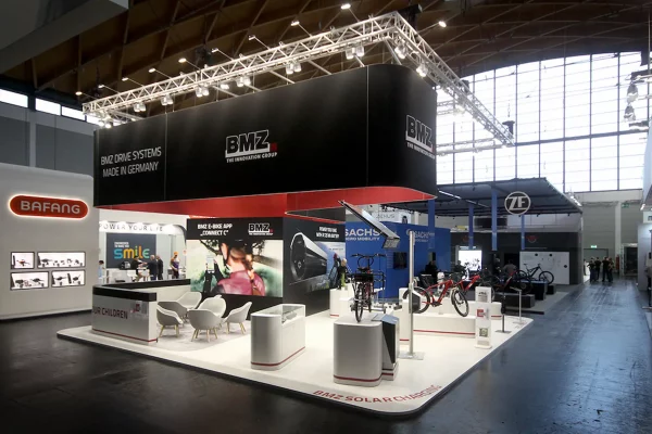 Messestand von BMZ Group mit Tischen, Stühlen.