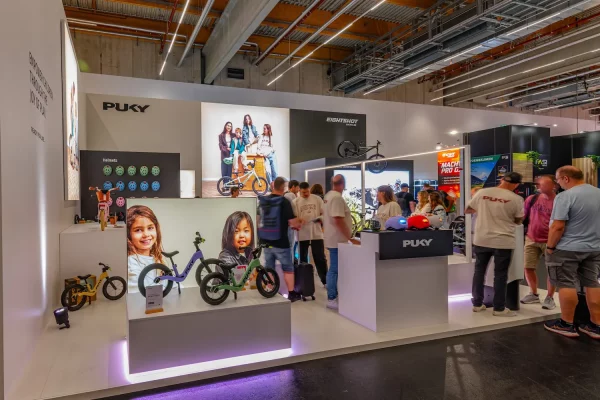 Zu sehen ist ein Messestand mit Kinderfahrrädern sowie Messebesucher.