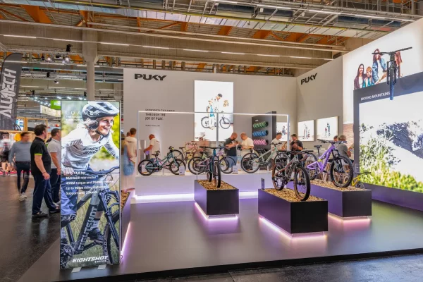Zu sehen ist ein Messestand, auf dem Kinderfahrräder auf Podesten ausgestellt sind.